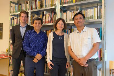 Eine Gruppe von vier Personen steht vor einem Bücherregal und lächelt in die Kamera. Eine Gruppe von vier Personen steht vor einem Bücherregal und lächelt in die Kamera.