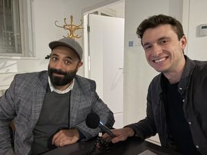 Zwei Männer sitzen nebeneinander und lächeln in die Kamera. Zwei Männer sitzen nebeneinander und lächeln in die Kamera.